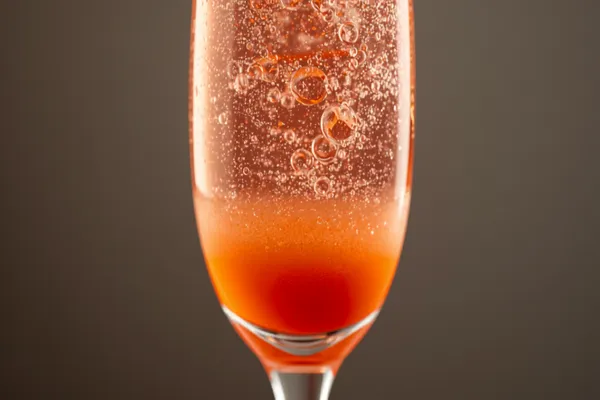 A Bellini in a champagne flute, soft pink-peach and gently sparkling, the colour graduating from the purée at the base.