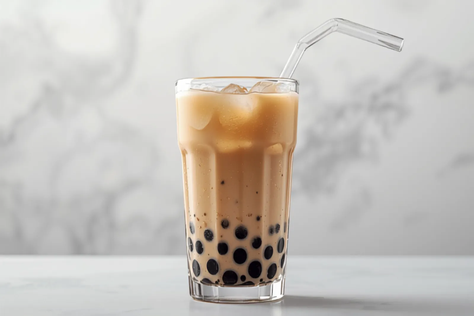 A clear glass of milky brown bubble tea with dark tapioca pearls settled at the bottom, ice, and a wide pink straw, bright modern light.