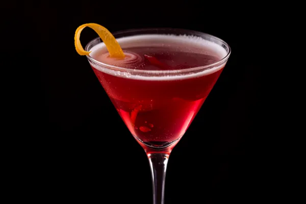 A deep-pink French Martini in a chilled martini glass with a delicate foam top and a lemon twist, glamorous soft light.