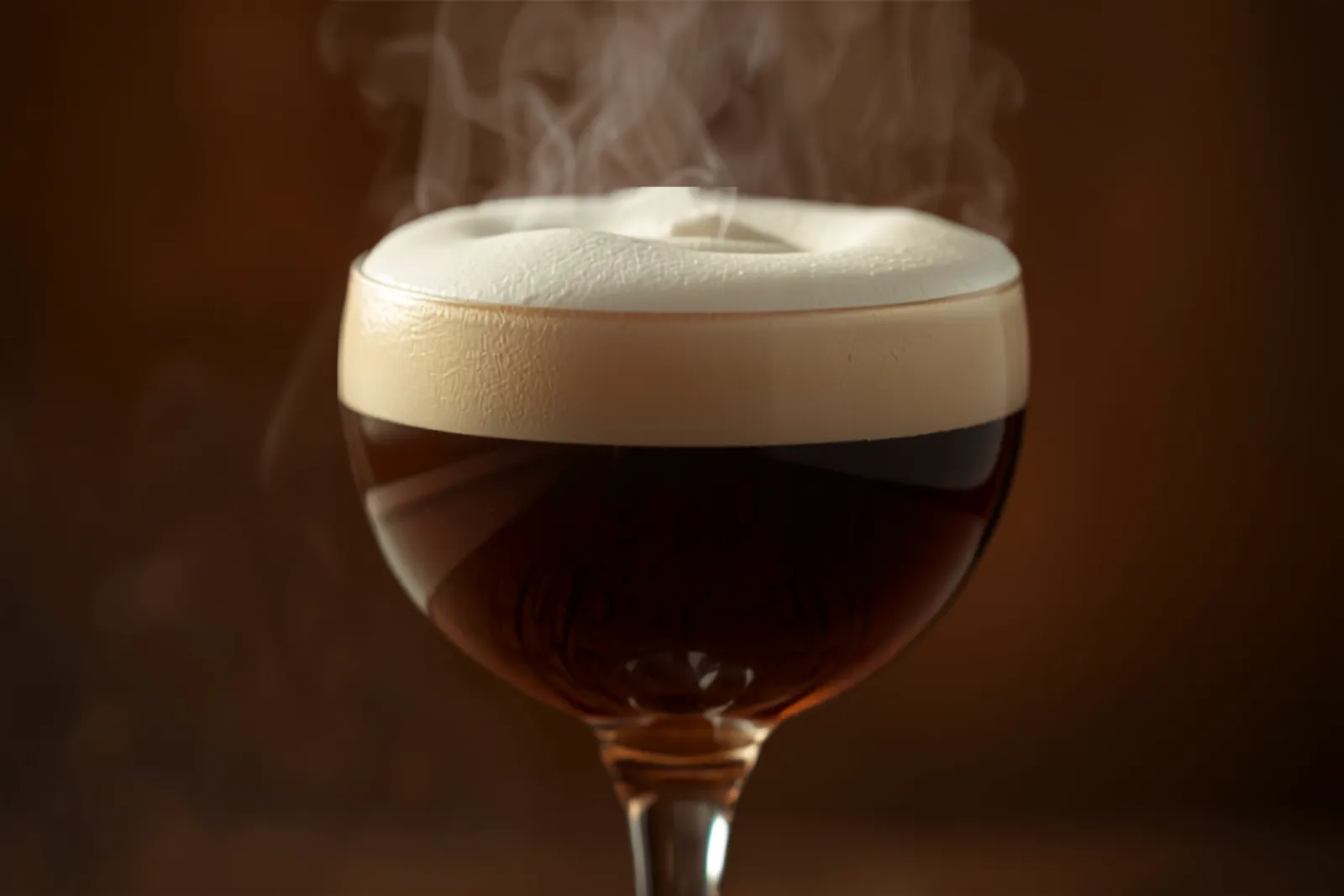 An Irish coffee in a clear stemmed glass — dark coffee below a thick collar of softly whipped cream, steam rising, warm light.