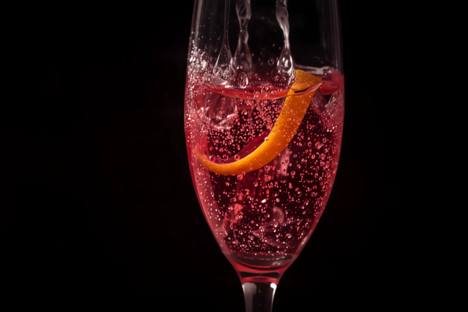 A jewel-pink Kir Royale in a champagne flute with fine bubbles and a lemon twist, elegant soft light.